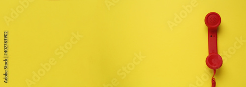 Hotline service. Red telephone receiver and space for text on yellow background, top view
