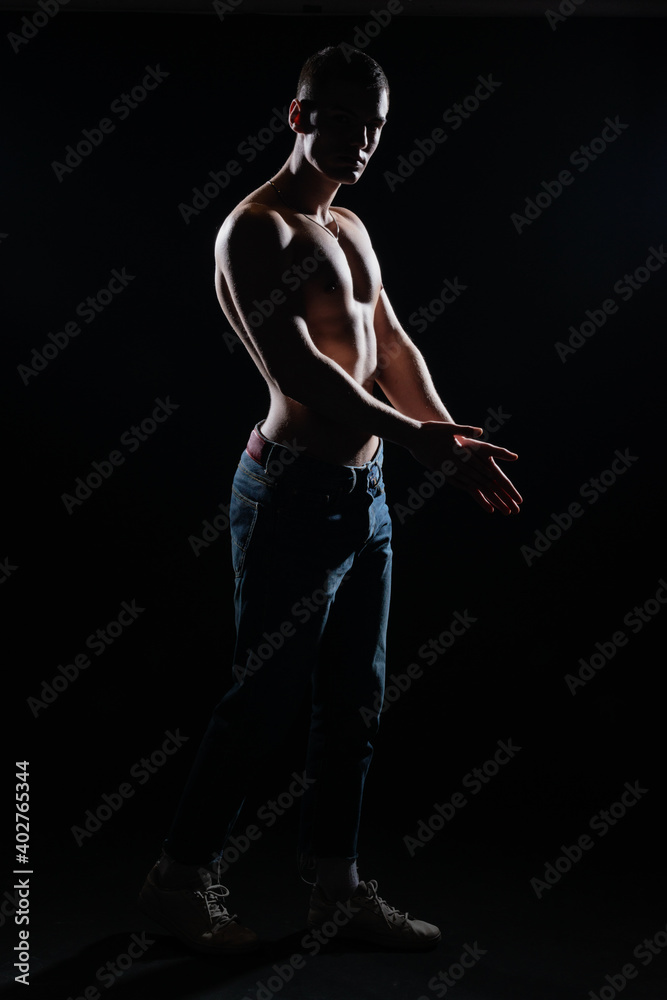 Silhouette picture of a hot shirtless muscular man posing in jeans in a dark studio.