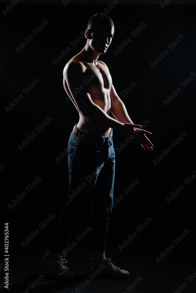Silhouette picture of a hot shirtless muscular man posing in jeans in a dark studio. Silhouette picture of a hot shirtless muscular man posing in jeans in a dark studio.