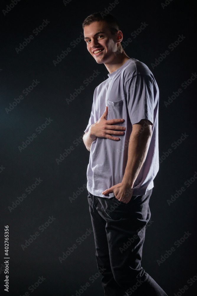 Naklejka premium Portrait of a smiling handsome young man wearing a gray t-shirt and black pants poses on black background in a studio