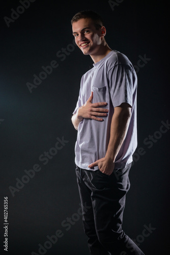 Portrait of a smiling handsome young man wearing a gray t-shirt and black pants poses on black background in a studio