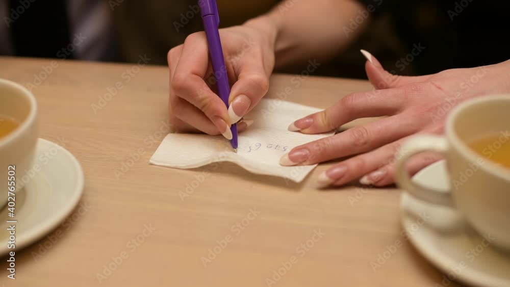 a woman writes her phone number on a napkin at a bar after meeting a man, close up