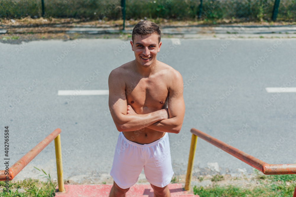 Fototapeta premium Portrait of a smiling handsome young athlete without t-shirt standing on stairs