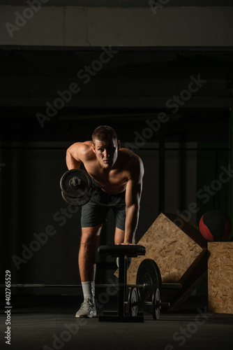 Sportsman doing exercises with weights over fitness bench and looking straight at the camera.