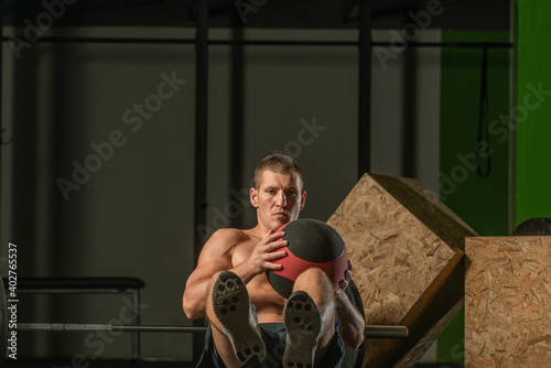 Close-up photo of a handsome bodybuilder working out seated using a medicine ball