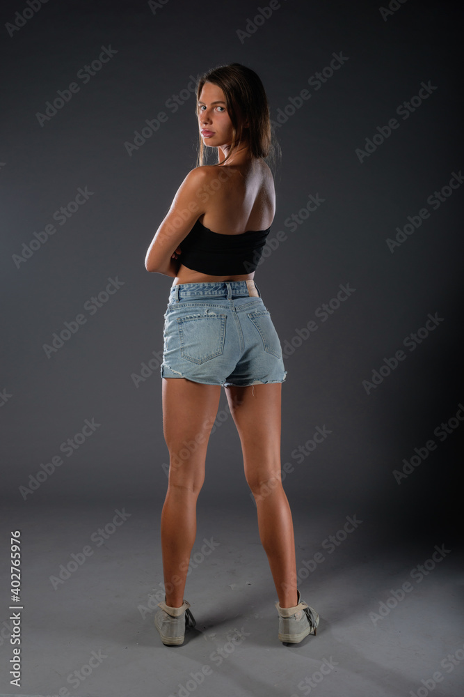 Beautiful young female model in short denim jeans on dark background. Beautiful young female model in short denim jeans on dark background.