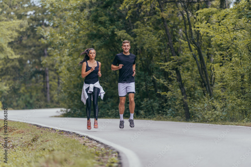 Young fit couple atheltes running on running road in a forest. Young fit couple atheltes running on running road in a forest.