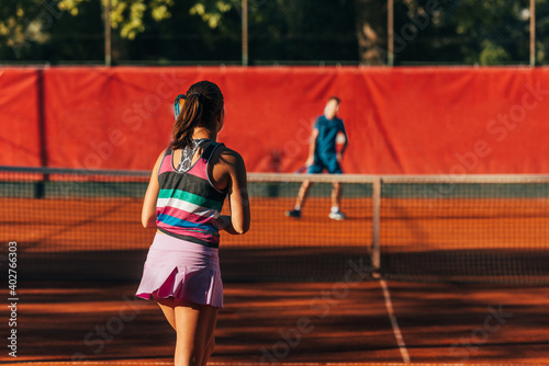 View from the back of a young female paying tennis on a court outside © qunica.com