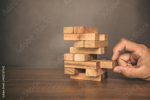 Close-up hand pull wooden block from other the wood block stacked in tower shape concepts of financial risk management and strategic planning.