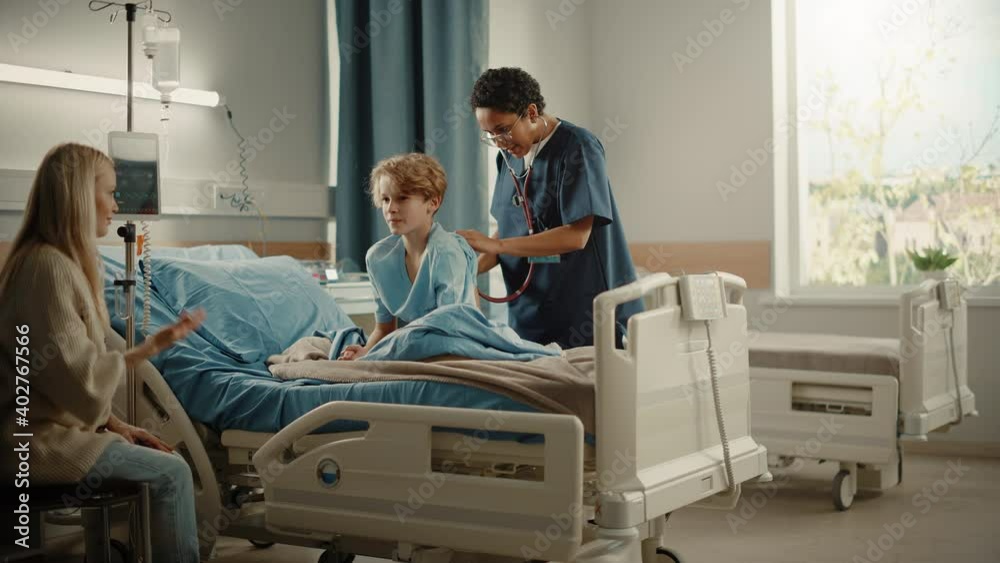 Hospital Ward: Handsome Young Boy Resting in Bed with Caring Mother Supporting Him, Friendly Head Nurse Listens to His Lungs, Heart Beat with Stethoscope. Doctor Does Checkup Happy Patient Recovering Hospital Ward: Handsome Young Boy Resting in Bed with Caring Mother Supporting Him, Friendly Head Nurse Listens to His Lungs, Heart Beat with Stethoscope. Doctor Does Checkup Happy Patient Recovering