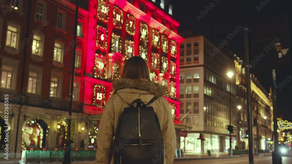 A tourist girl with backpack walking at night on decorated with lights city streets in 4K. Concept of a young female exploring big empty city during the night with colorful lights on the buildings. A tourist girl with backpack walking at night on decorated with lights city streets in 4K. Concept of a young female exploring big empty city during the night with colorful lights on the buildings.