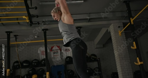 Muscular sportswoman doing burpee exercise. Tracking shot of blond female athlete doing squat thrust exercise during intense workout in gym