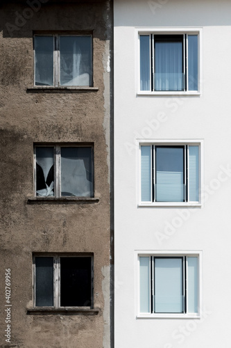 Facade of a white restructured house next to the old original front with old brown plaster and broken window glass © 1take1shot