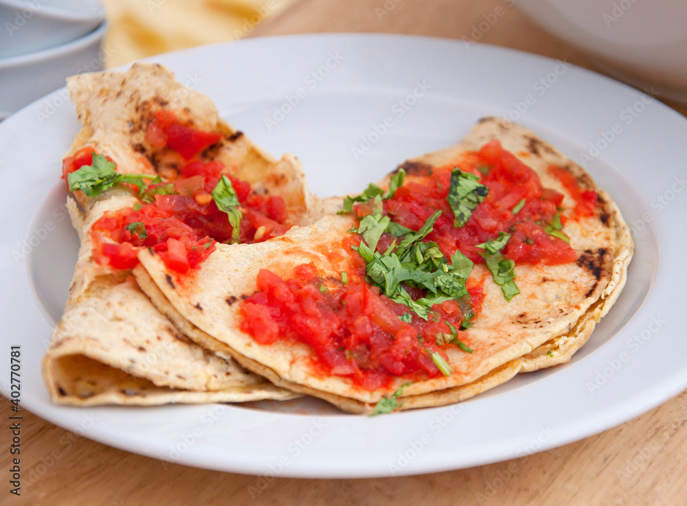 Serving plate with corn pancakes, tomato sauce and herbs