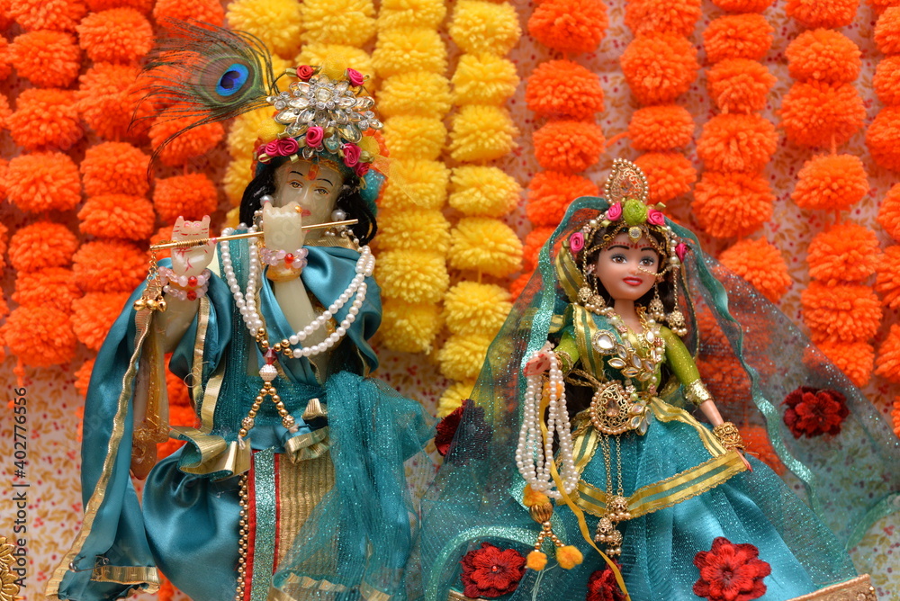 Idol of Krishna and Radha beautifully dressed and decorated in colorful attire and jewelry, with a background of orange and yellow flowers, shot in landscape composition