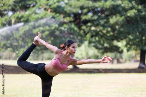 Asian woman doing yoga with stretching arms and leg outdoor in the park. Woman wearing sportswear and working out outdoor. Yoga and exercise outdoor concept