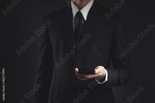 Businessman showing smart phone in black suit.