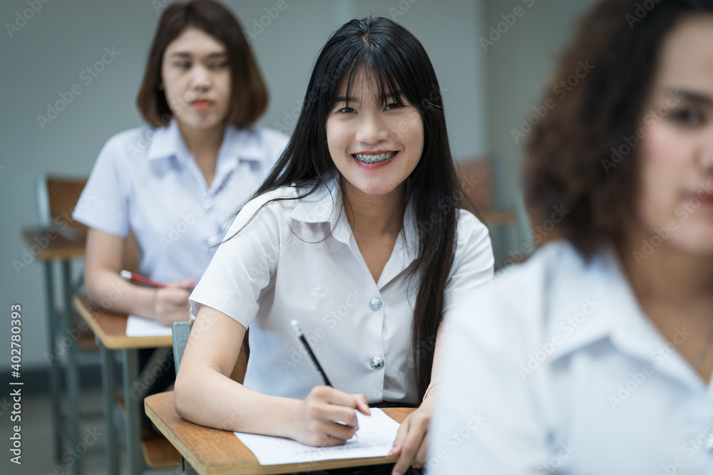 Portrait of cheerful Asian female college students writing and studying in the classroom. Selective focus teenage university students studying in classroom.