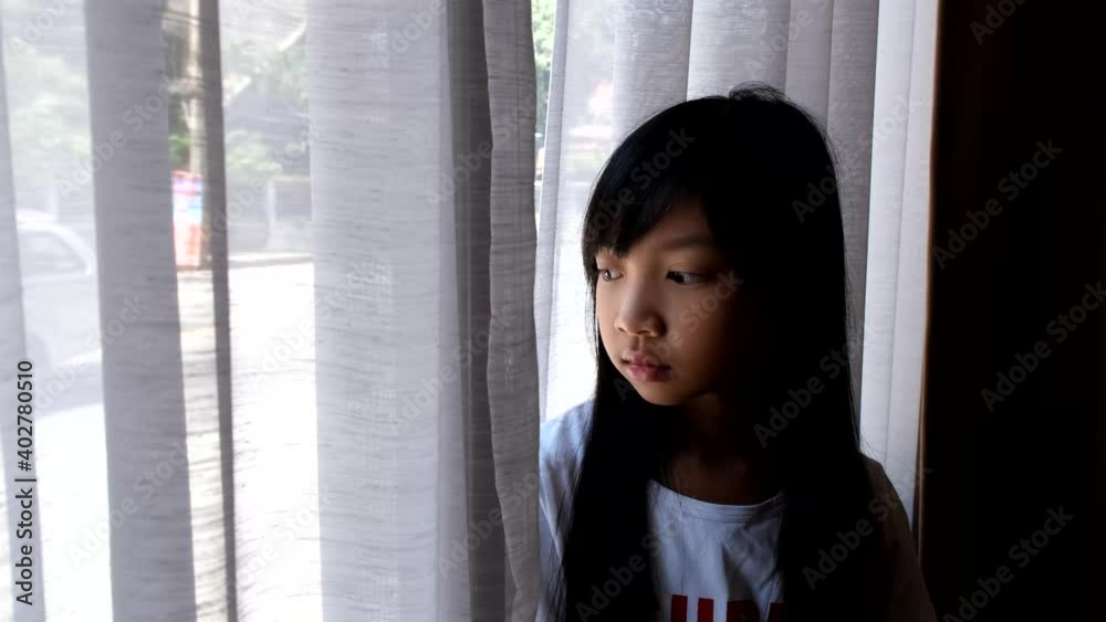 A young Asian girl in a white T-shirt is looking out of the window. A young Asian girl in a white T-shirt is looking out of the window.