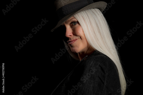 Image of a beautiful mature woman with platinum blonde hair, wearing a hat. Studio image with a black background.