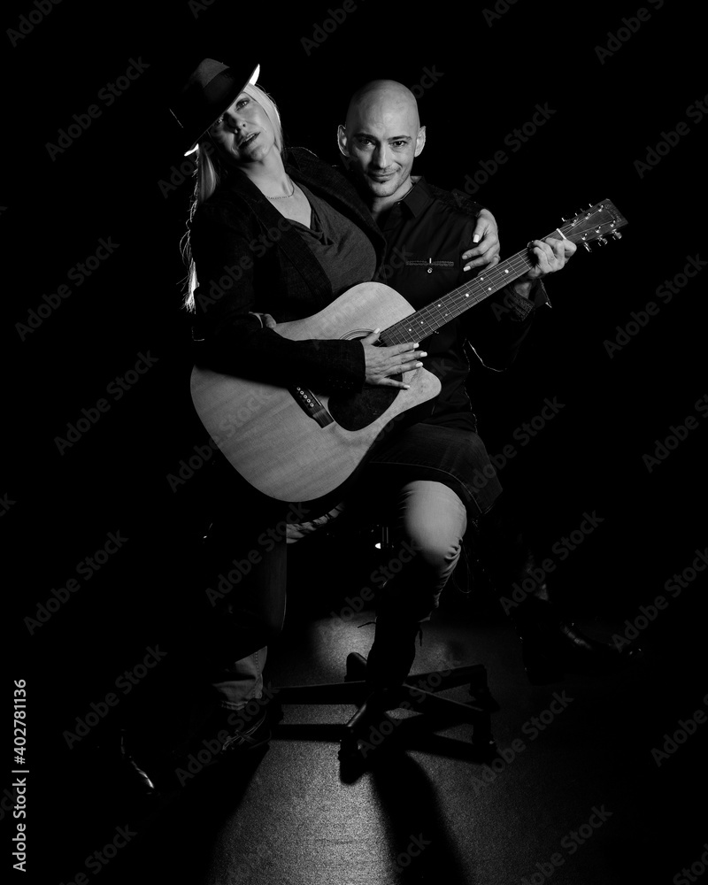Image of a man and woman sitting in a dark room holding a guitar, creating art and music. Image of a man and woman sitting in a dark room holding a guitar, creating art and music.