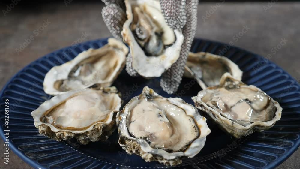 Seafood restaurant. Skilled chef in gloves lays delicious raw ocean oyster on round plate. closeup view. Serving food. Slow motion. Full hd Seafood restaurant. Skilled chef in gloves lays delicious raw ocean oyster on round plate. closeup view. Serving food. Slow motion. Full hd