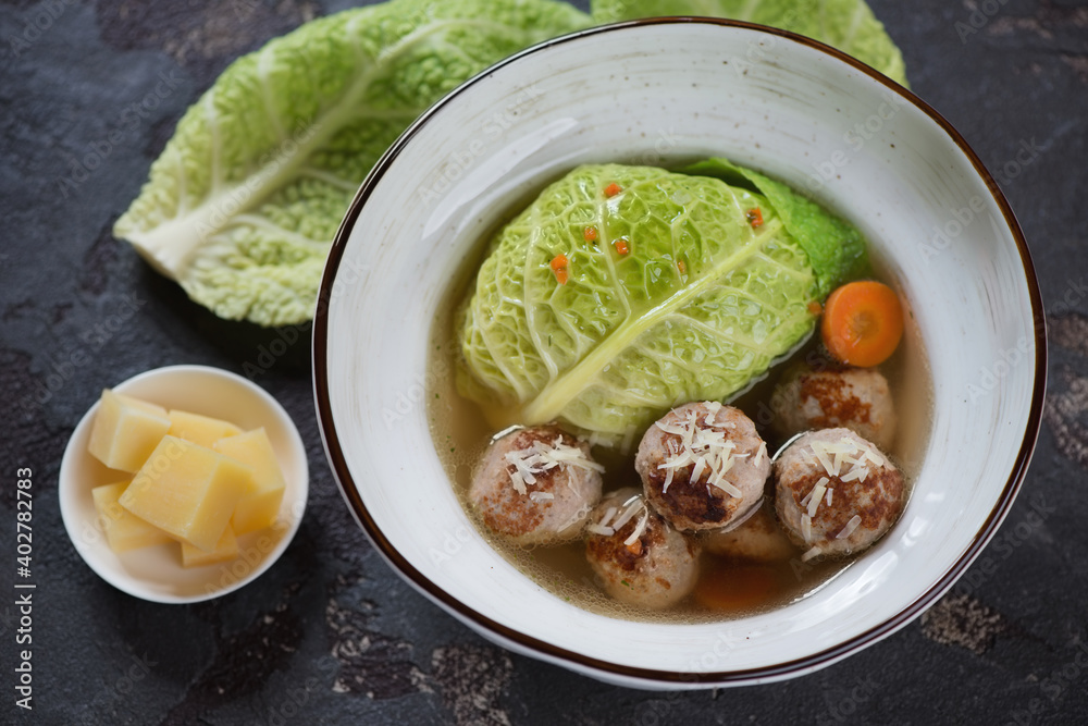 Soup with meatballs and savoy cabbage served in a white bowl over brown stone background, horizontal shot