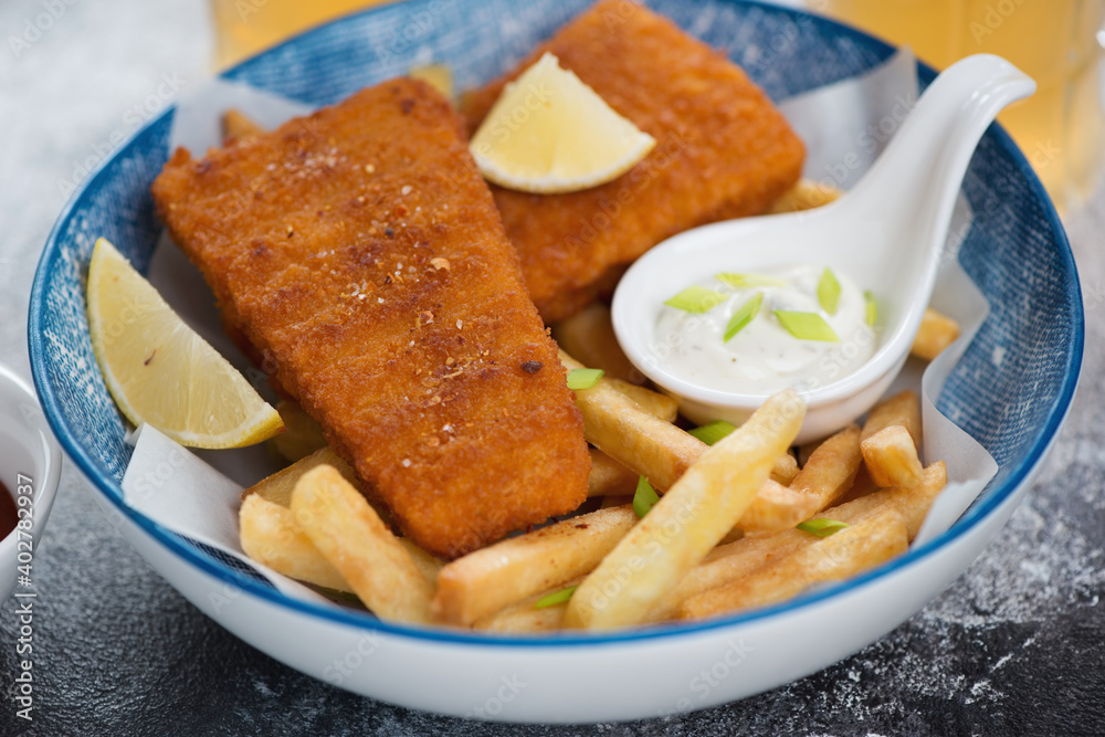 Deep-fried breaded fish fillet with french fries and dips in a blue bowl, close-up, studio shot Deep-fried breaded fish fillet with french fries and dips in a blue bowl, close-up, studio shot