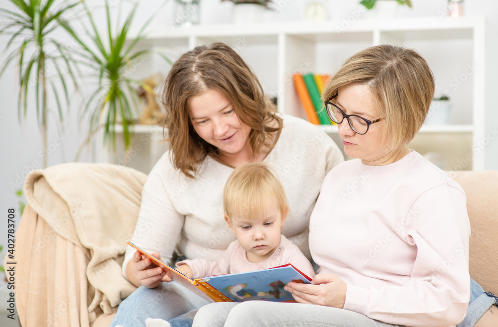 Female couple sitting on the sofa of their front room with their child, readding her a book