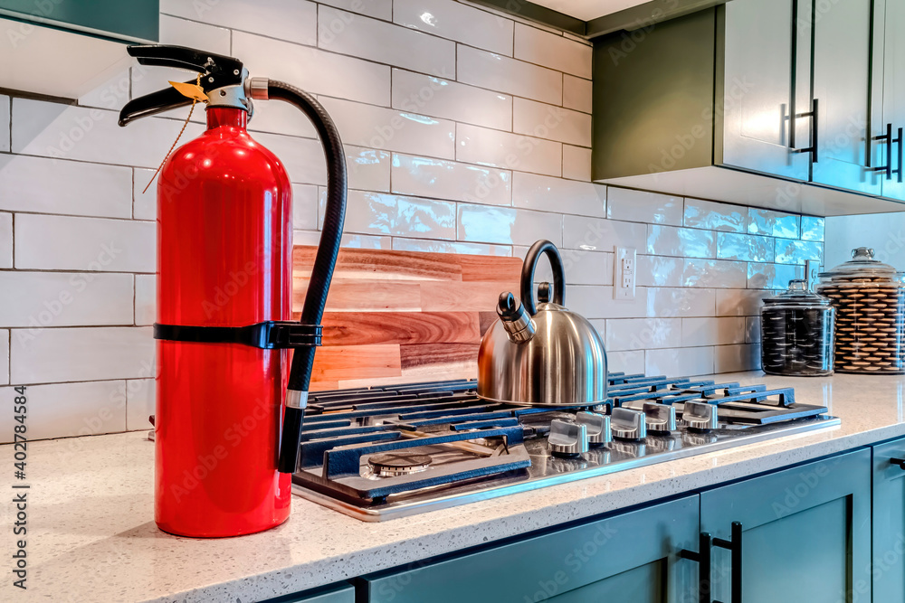 Fire extinguisher and cooktop with kettle on the countertop inside home kitchen Fire extinguisher and cooktop with kettle on the countertop inside home kitchen