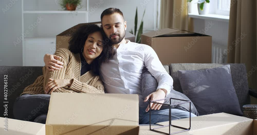 Interracial couple curly beautiful young wife and bearded attractive newlyweds husband sleeping surrounded by cardboard boxes parcels tired after moving to new apartment, real estate purchase concept Interracial couple curly beautiful young wife and bearded attractive newlyweds husband sleeping surrounded by cardboard boxes parcels tired after moving to new apartment, real estate purchase concept