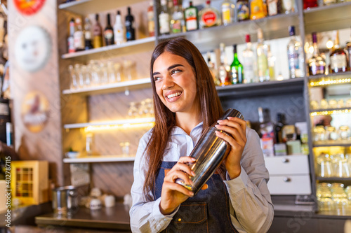 Young female worker at bartender desk in restaurant bar preparing coctail with shaker. beautiful young woman behind bar making coctail photo