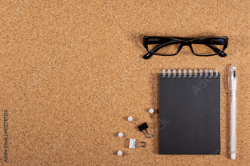 Black glasses and a black notebook on a cork board