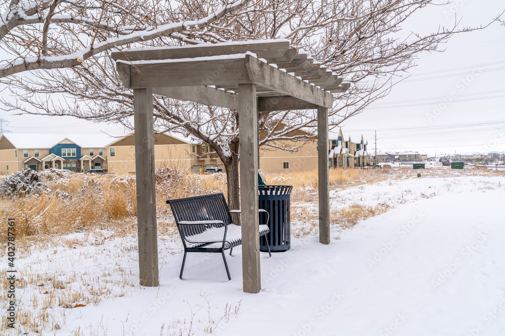 Bench and garbage can under wooden pergola against homes sky and leafless tree Bench and garbage can under wooden pergola against homes sky and leafless tree