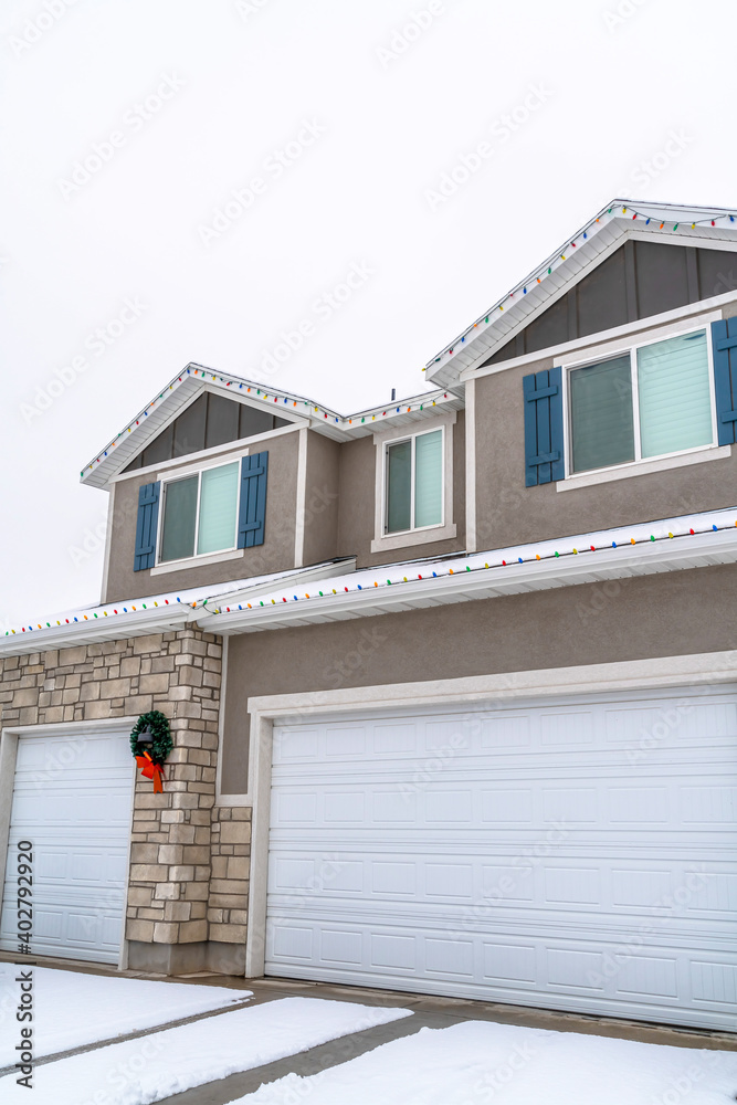 White garage doors at home exterior decorated with wreath and christmas lights