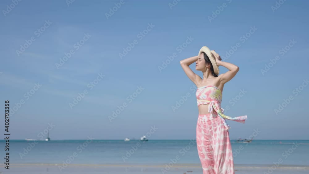 Young beautiful asian woman in summer clothes wearing hat walking on the beach with a sea on background. pretty girl on vacation at tropical island. Wind blows fresh air, slow motion win blowing hat Young beautiful asian woman in summer clothes wearing hat walking on the beach with a sea on background. pretty girl on vacation at tropical island. Wind blows fresh air, slow motion win blowing hat