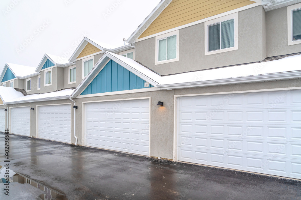 Back view of apartments with white garage doors and snowy roofs in winter