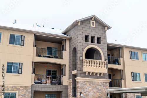 Three storey residential building with balcony and snowy roof against white sky