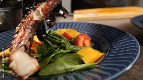 Serving gourmet dish with octopus in high end luxury restaurant. Delicious seafood cooking. Chef putting delicious grilled octopus tentacle on plate in slow motion. Full hd