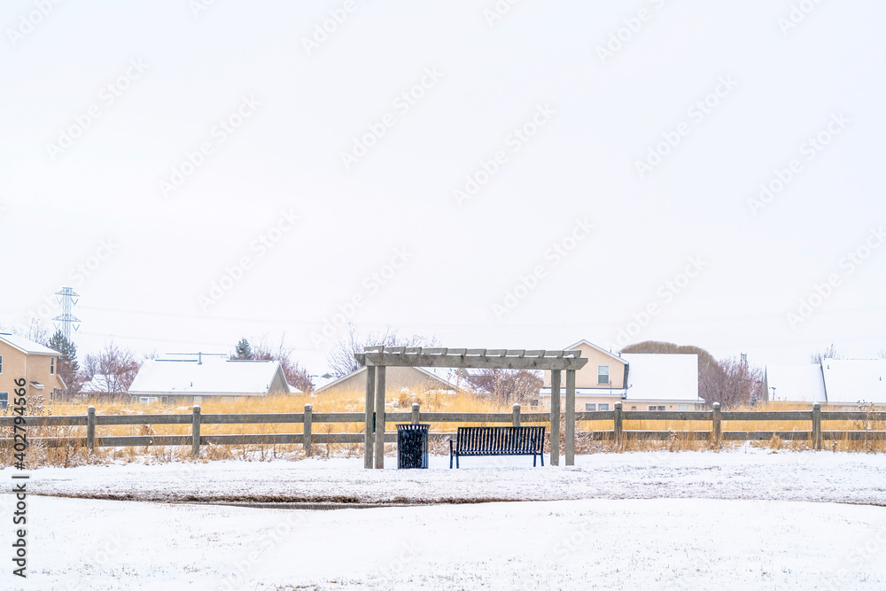 Snowy landscape in winter with bench under pergola against vast overcast sky Snowy landscape in winter with bench under pergola against vast overcast sky