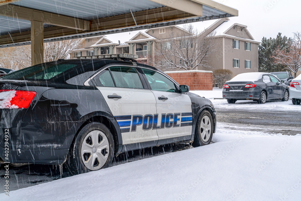 Black and white police car parked in the neighborhood on a snowy and rainy day Black and white police car parked in the neighborhood on a snowy and rainy day