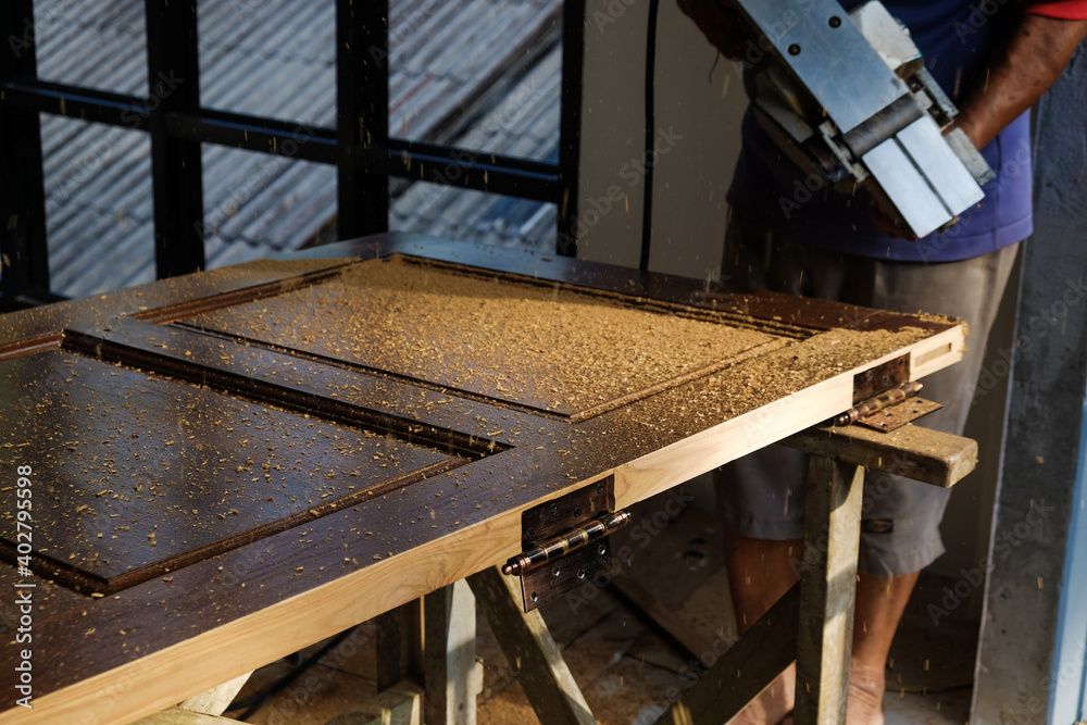 Carpenter works with a electric planer in a workshop for the production of vintage teak wood door Carpenter works with a electric planer in a workshop for the production of vintage teak wood door