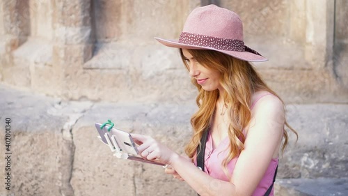 Young woman sitting on the ground checking her phone. Girl using social media apps on  smatphone outdoors. Tourist in Barcelona playing with her cellphone,  photo