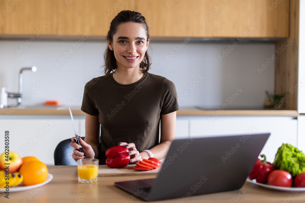 Young woman enjoying cooking looking for a recipe on the laptop in the kitchen