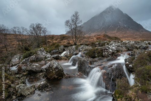 Epic landscape image of Buachaille Etive Mor waterfall in Scottish highlands on a Winter morning with long exposure for smooth flowing water