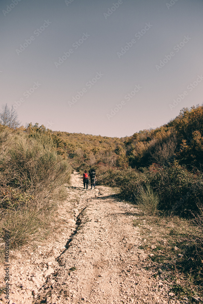 Mountain path with two young walkers with backpack climbing the road with stones and vegetation