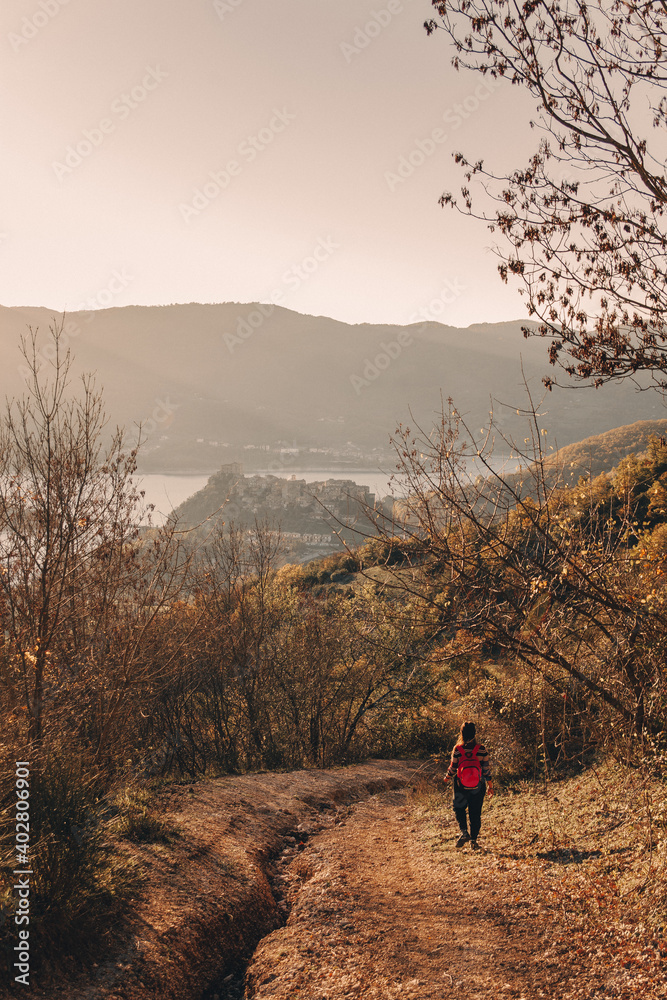 Young girl walks with backpack along a mountain path at sunset in autumn