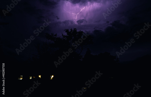sky with lightening snd a house with light lit windows 
