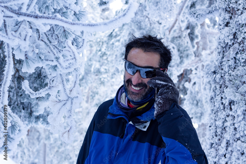 Man talking by smartphone smiling in a snowy landscape.Communication concept in any location.Telephone connection Man talking by smartphone smiling in a snowy landscape.Communication concept in any location.Telephone connection