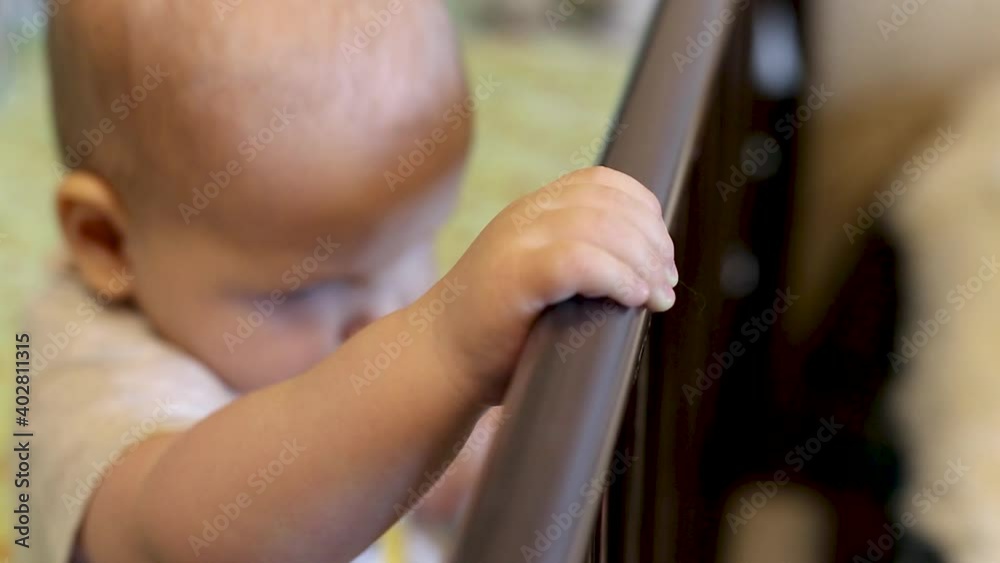 A small child is held on the side of the cot, close-up. A small child is held on the side of the cot, close-up.